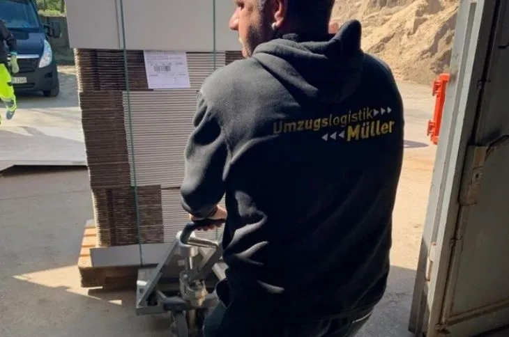 umzugshelfer transportiert palettierte ware mit hubwagen
